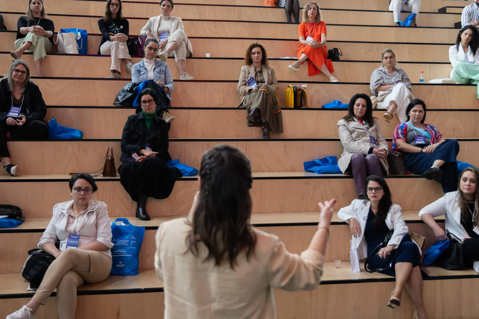 Encontro presencial da NEUROARQ®: participantes sentadas numa arquibancada de madeira ouvem uma palestrante.